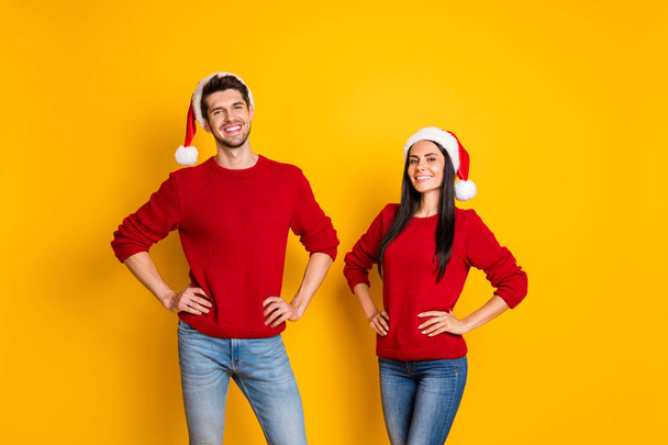 Portrait of cheerful spouses in santa claus hats look stand isolated over yellow background - Foto, Bild