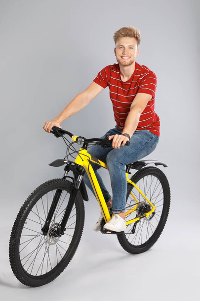 Handsome young man riding bicycle on grey background - Zdjęcie, obraz