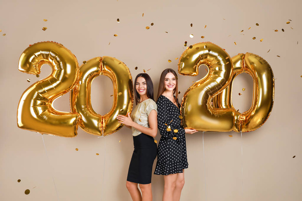 Happy young women with golden 2020 balloons on beige background. New Year celebration - Fotó, kép