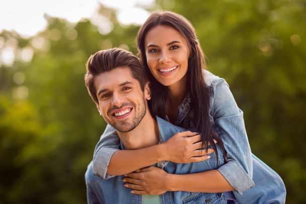 Close up photo of charming couple piggyback wearing denim jeans outdoors - Foto, afbeelding