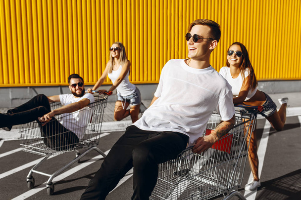 A group of happy young people, having fun on shopping carts, ride on a shopping cart. summer day with sunlight. - Photo, image