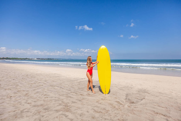 Girl in red swimsuit holding the surfboard standing alone on the Bali beach - Foto, Imagem