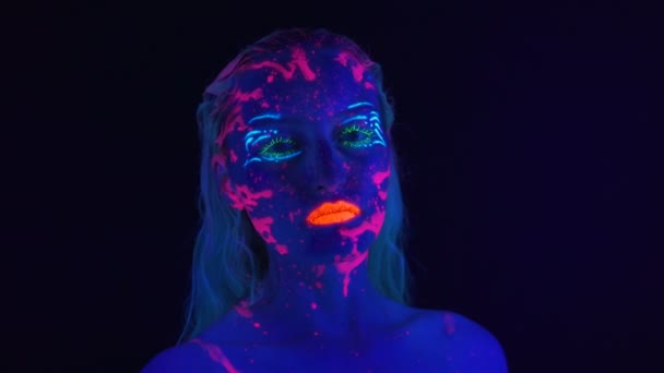 Молодая женщина с ярким макияжем в ультрафиолетовом свете - Кадры, видео