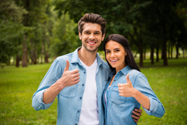 Portrait of lovely couple with brunet hair showing thumb up smiling wearing jeans denim shirts jackets outside in forest - Fotoğraf, Görsel