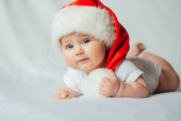 Carino piccolo bambino in cappello di Babbo Natale posa su pancia su sfondo bianco
 - Foto, immagini