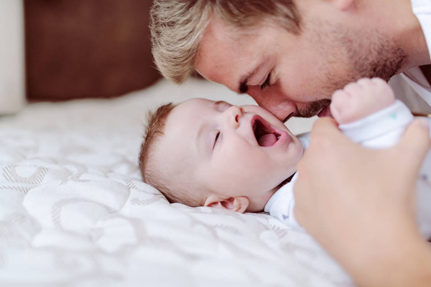 Slaperig schattig Kaukasische SIC maanden oude baby jongen liggend in bed en geeuwen. Zijn vader knuffelen hem. NAP-tijd. - Foto, afbeelding