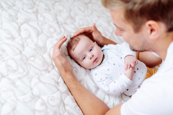 Yakışıklı genç baba oynarken ve onun sevimli altı aylık oğlu konuşurken üst görünümü. Yatakta yatarken uzağa bakan bebek. - Fotoğraf, Görsel