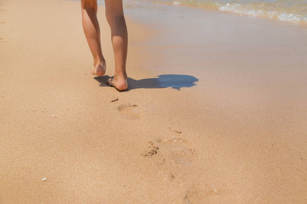 Kind spaziert am Strand entlang und hinterlässt Spuren im Sand. Selektiver Fokus. - Foto, Bild