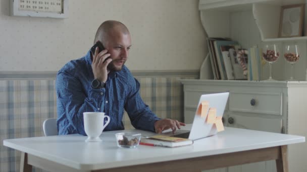 Jeune freelance masculin travaillant à l'ordinateur portable et smartphone assis à la table avec du thé et des collations
  - Séquence, vidéo
