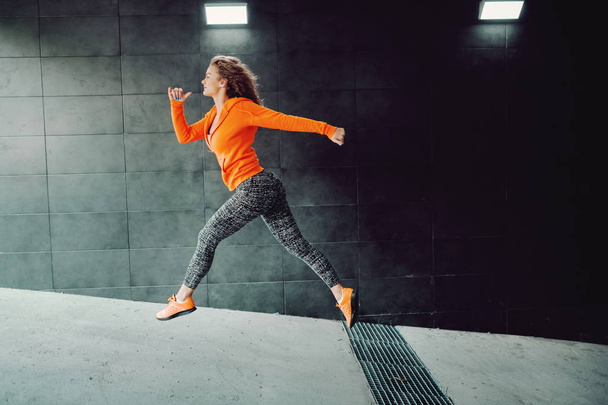 Vista lateral de la mujer caucásica en forma de ropa deportiva corriendo en pasaje. concepto de estilo de vida saludable
. - Foto, imagen