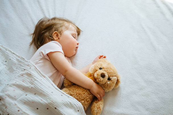 Little baby sleeping on bed embracing soft toy, free space - Фото, изображение