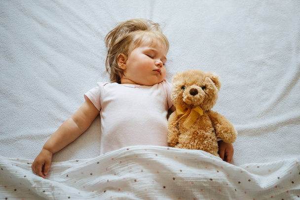 Kleines Baby, das auf dem Bett schläft, umarmt Stoffbär, weißer Hintergrund - Foto, Bild