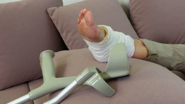 Woman's injured leg and crutches on couch close up - Séquence, vidéo