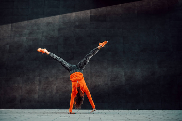 Full length of fit sporty caucasian woman in sportswear doing cartwheel exercise in front of black wall. - Photo, Image