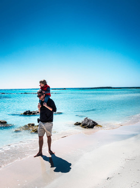 Père portant son fils sur l'épaule à la plage
 - Photo, image