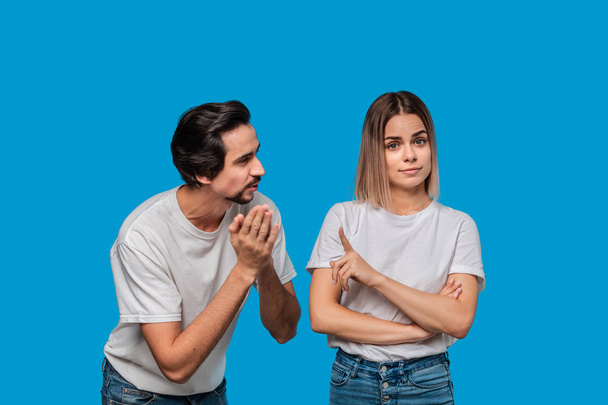 Brunet bearded man with mustaches in white t-shirt and blue jeans asking his girlfriend for forgiveness isolated over blue background. Concept of guilt. - Foto, Bild