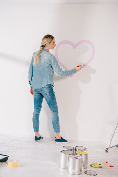pretty young woman drawing heart with pink paint on white wall - Foto, Imagem