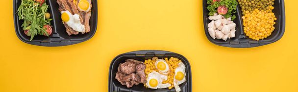 tiro panorâmico de pacotes ecológicos com legumes, carne, ovos fritos e saladas isoladas em amarelo
     - Foto, Imagem
