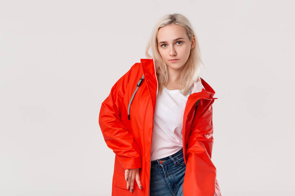 Pretty blond girl in a red raincoat standing isolated over white background. Get ready for bad weather. - Photo, Image
