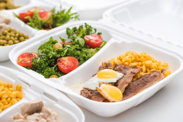 selektiver Fokus des Ökopakets mit Mais, Fleisch, Spiegeleiern und Salat auf weißem Hintergrund  - Foto, Bild
