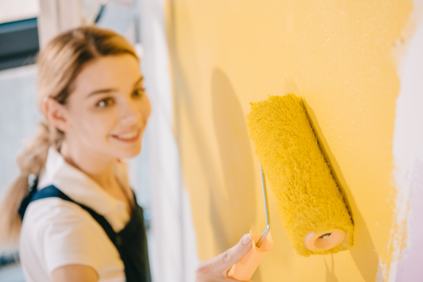 Genç ressamın seçici odak noktası boya silindiriyle duvarı sarıya boyamak - Fotoğraf, Görsel