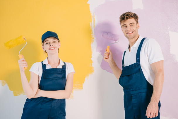 Junge Maler in Overalls halten Farbwalzen in der Hand und lächeln in die Kamera - Foto, Bild