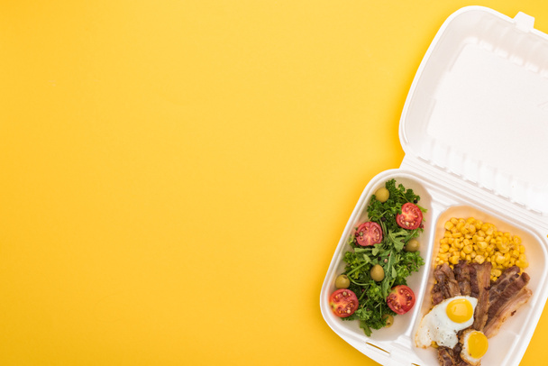 top view of eco package with corn, meat, fried eggs and salad isolated on yellow  - Photo, Image