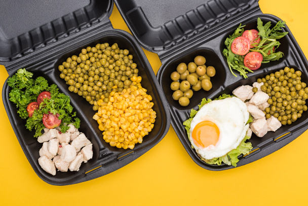 vista dall'alto di confezioni ecologiche con verdure, carne, uova fritte e insalate isolate sul giallo
  - Foto, immagini