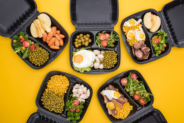 bovenaanzicht van eco-pakketten met appels, groenten, vlees, gebakken eieren en salades geïsoleerd op geel  - Foto, afbeelding