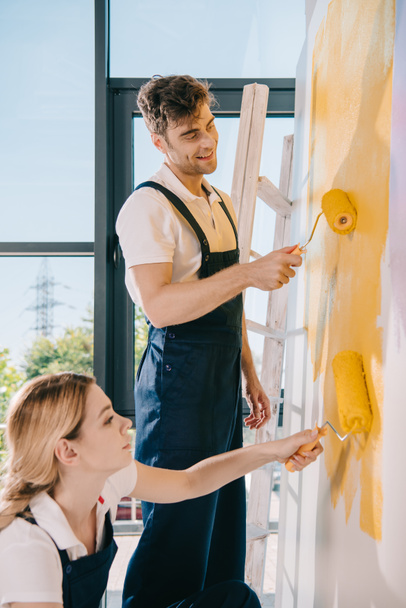 dos jóvenes pintores pintando la pared en amarillo con rodillos de pintura
 - Foto, Imagen
