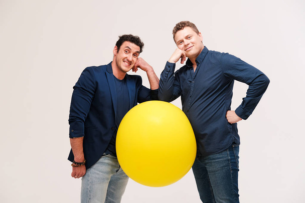 studio portrait of two men posing with big yellow ball against plain background - Foto, Imagem