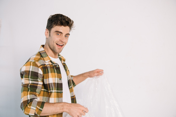 smiling young man holding cellophane while preparing for wall painting - Fotografie, Obrázek
