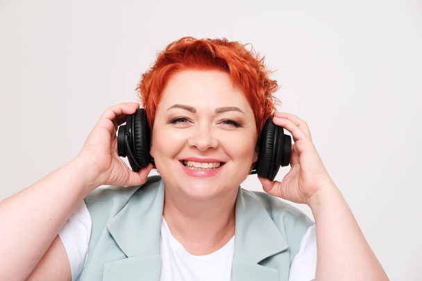 studio portrait of excited redhead woman listening music in headphones on plain background - Photo, image