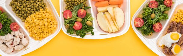 tiro panorâmico de pacotes ecológicos com legumes, maçãs, carne, ovos fritos e saladas isoladas em amarelo
     - Foto, Imagem