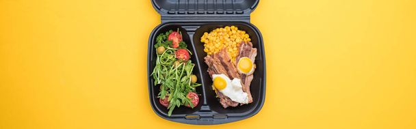 πανοραμική λήψη της οικολογικής συσκευασίας με καλαμπόκι, κρέας, τηγανητά αυγά και σαλάτα που απομονώνονται σε κίτρινο     - Φωτογραφία, εικόνα