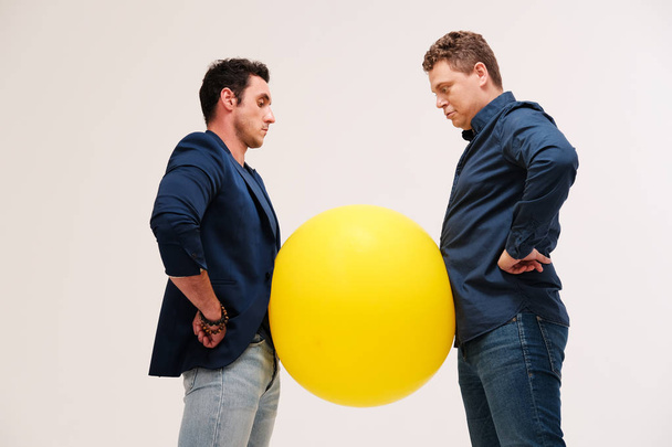 studio portrait of two men posing with big yellow ball against plain background - 写真・画像