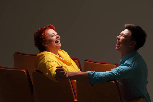 studio portrait of cheerful couple holding hands and sitting on chairs  - Foto, Imagem