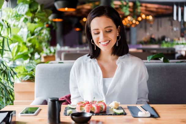 cheerful woman looking at tasty sushi in sushi bar  - 写真・画像