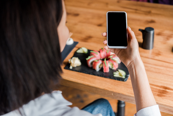 selective focus of woman holding smartphone with blank screen near tasty sushi in restaurant  - Photo, Image