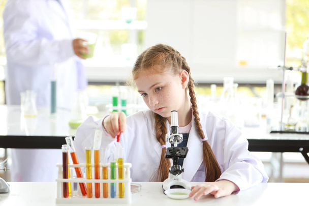 цікава дівчинка експериментує з наукою, скидаючи рідину в пробірку з мікроскопом і обличчям уваги (освіта і концепція вченого
) - Фото, зображення