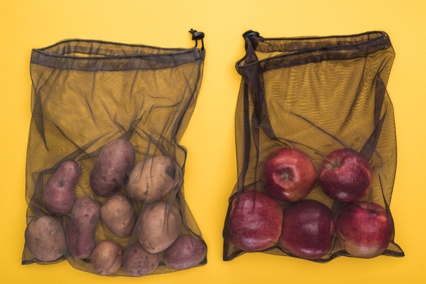 top view of potatoes and apples in eco friendly black mesh bags isolated on yellow - Photo, Image