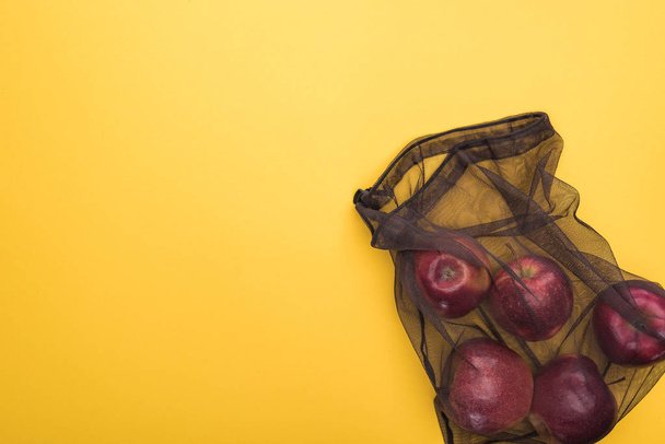 top view of apples in eco friendly black mesh bag isolated on yellow - Foto, immagini