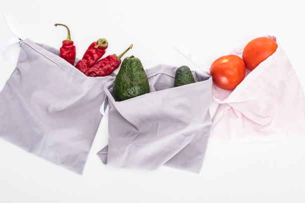 top view of fresh avocados, tomatoes and chili peppers in eco friendly bags isolated on white - Fotó, kép