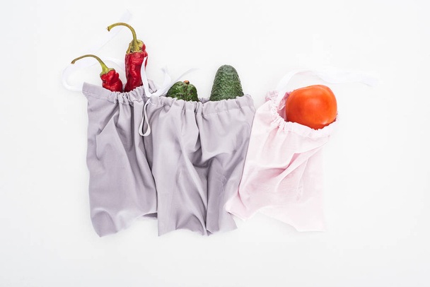 top view of fresh avocados, tomatoes and chili peppers in eco friendly bags isolated on white - 写真・画像