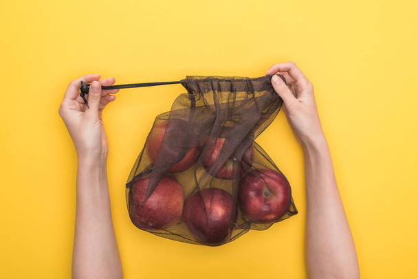 cropped view of woman holding eco friendly bag with ripe apples isolated on yellow - Фото, зображення