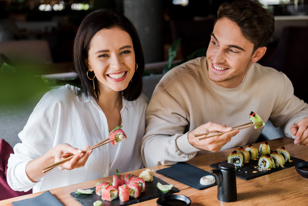 felice uomo e donna in possesso di bacchette con sushi gustoso nel ristorante
  - Foto, immagini