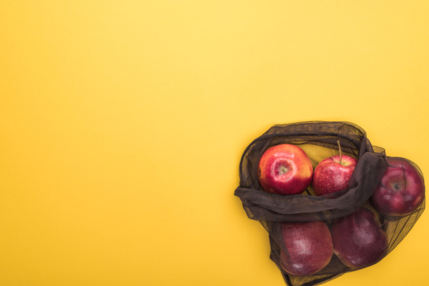 top view of ripe apples in black eco friendly bag isolated on yellow - 写真・画像