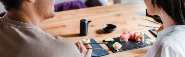 panoramic shot of man holding chopsticks near young woman in sushi bar - Photo, image