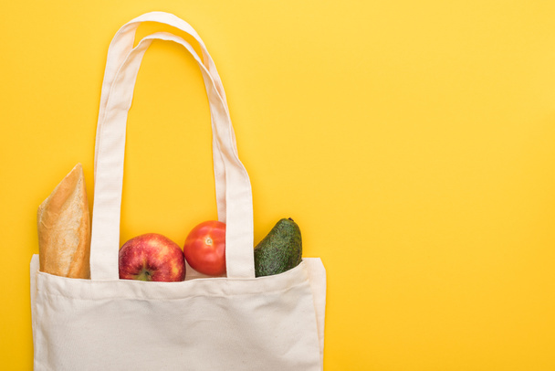 top view of ripe apples, baguette and avocado in eco friendly bags isolated on yellow - Photo, Image