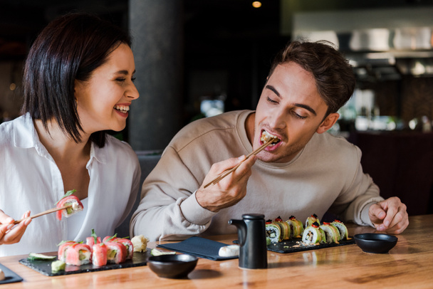 selective focus of man holding chopsticks while eating sushi near happy woman in sushi bar - Photo, image